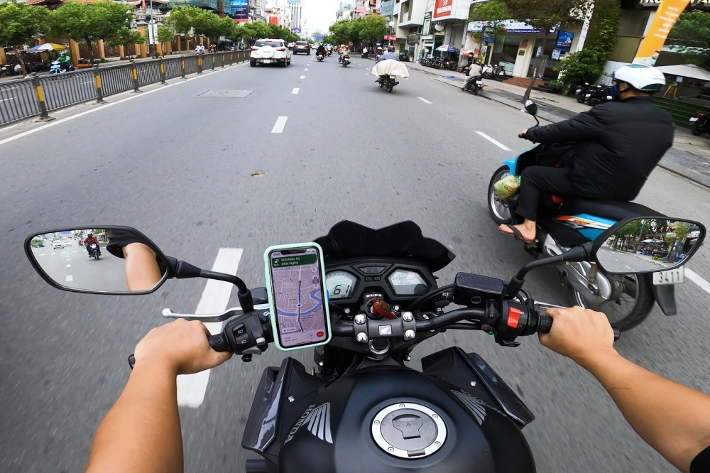 Một tay lái xe máy, điện thoại gắn trên giá đỡ, chạy trên đường