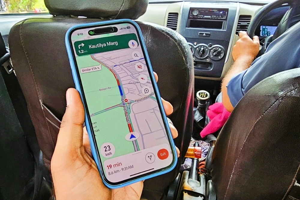 Một người đang so sánh các ứng dụng trên điện thoại với hình ảnh xe hơi ở nền sau