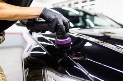 Một người đang sử dụng máy đánh bóng trên thân xe, tập trung vào khu vực có vết xước