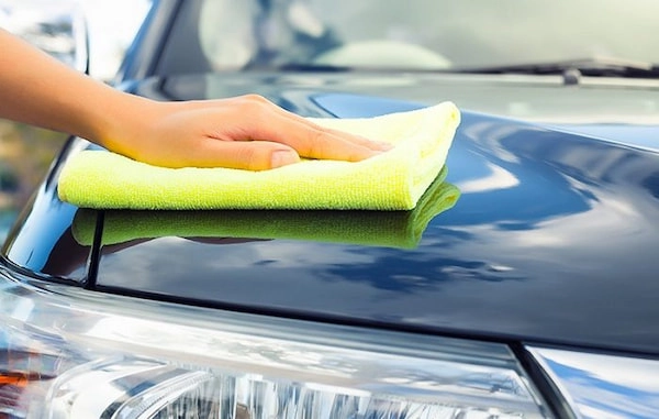 Một người đang sử dụng khăn microfiber và dung dịch đánh bóng để xử lý vết xước trên xe